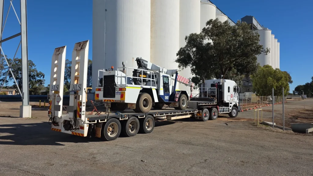 ALS International float carrying a mobile crane parked at a silo industrial site