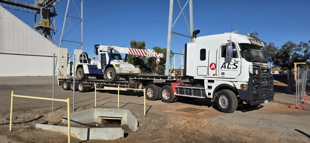 ALS International truck transporting a Franna pick-and-carry crane on a float at a grain terminal