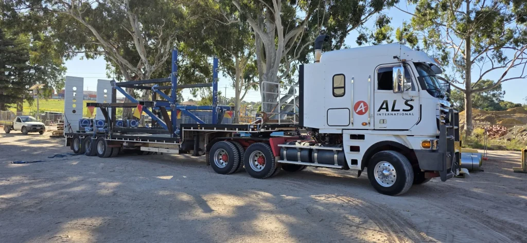 ALS International float transporting a blue machinery frame past gum trees