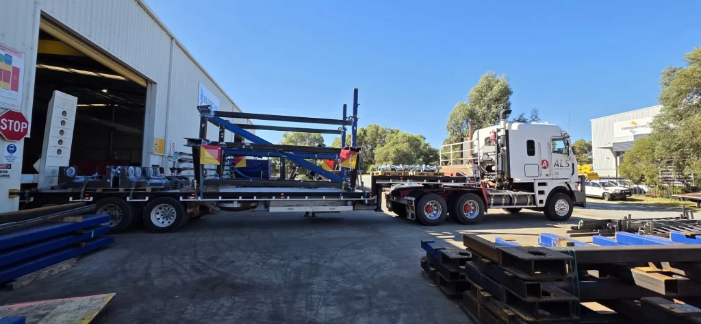 Steel frame being loaded onto an ALS International trailer outside a fabrication workshop