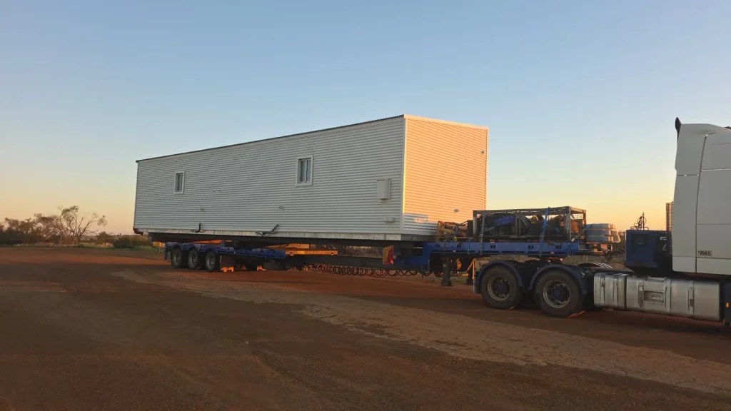 Transportable building module loaded on an ALS International trailer at dusk